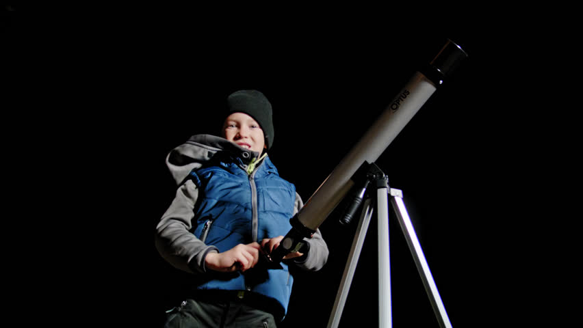 static shot of a young boy looking through telescope with a black background