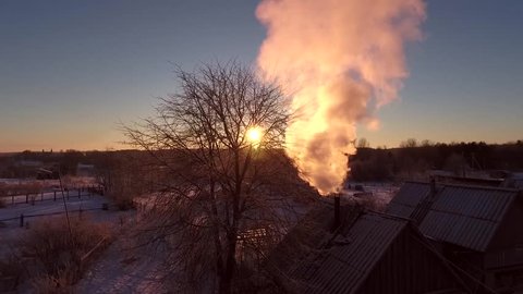Aerial view of smoke rising from the chimney of a wooden house in the countryside in the winter in the bitter cold at sunset