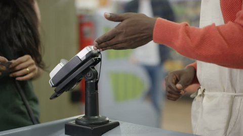 4K Friendly cashier taking payment from a customer at grocery store checkout Dec 2016-UK