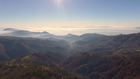 Aerial shot , gorgeous hills in the morning fog, sun high in the sky and beautiful autumn colors, filmed with drone