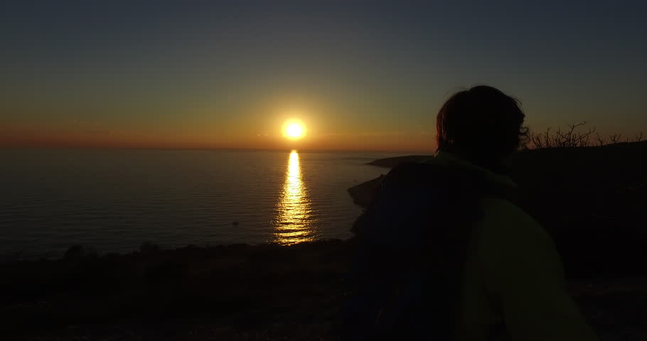 Hiker walking on the mountain peak above the sea at the sunset