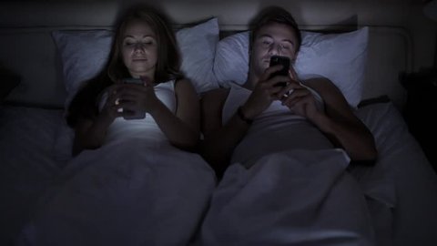 hotel, technology, intermet and happiness concept - smiling couple in bed with smartphones