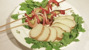 Delicious baked potatoes with bacon and cucumbers on skewers on plate. Video shows a dish, decorated with green