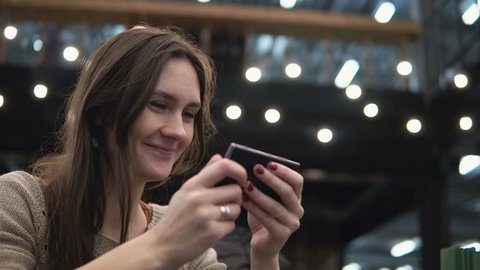 Closeup portrait. Woman using her smartphon touchscreen device in modern cafe lights in the background 4k