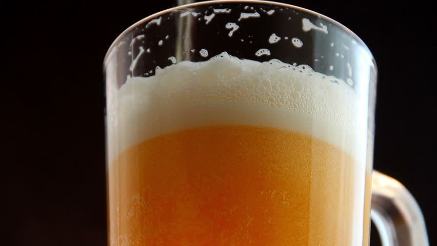 Mug full of beer in glass on a black background. Counter clockwise rotation of