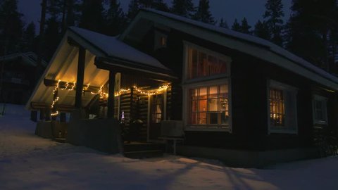 Moving at winter night by cozy wooden house in snowy forest village situated on lake shore in Finland .
