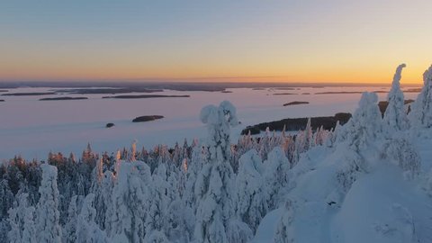Aerial nordic winter landscape flight over snow mountain forest on sunset.