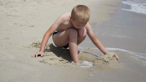boy buries leg in the sand/Boy on the beach buries leg in the sand