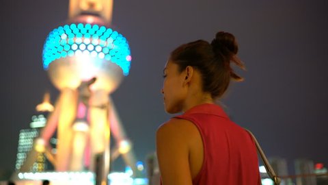 Shanghai business woman walking under the city lights at night by Oriental Pearl Tower in Pudong, China. Multicultural Asian Chinese / Caucasian young woman professional in financial district.
