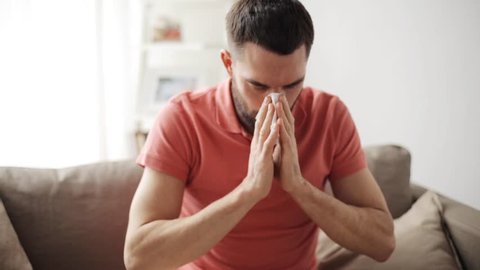 healthcare, flu, hygiene and people concept - sick man blowing nose to paper napkin at home
