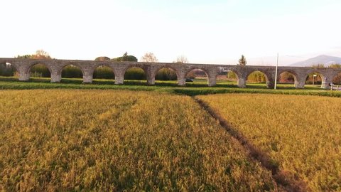 Aerial shot, foggy fields, an ancient roman aqueduct and cars driving behind it, filmed with drone