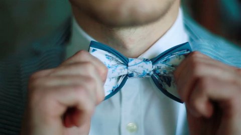 Wearing bow tie close up. Male hands check correct and adjust casual blue bow tie handmade from printed fabrics shallow depth of field. Elegant accessories male fashion macho dandy gentleman concept