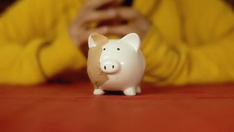 Grabbing a piggybank (a porcelain container for money, a small bank, shaped as a pig, with a slot at the top to receive coins) full of patches.
