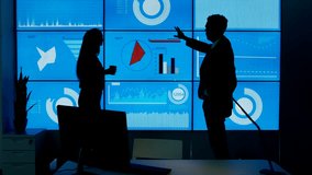 4K Business man & woman in modern office, silhouetted against large video wall Dec 2016-UK
