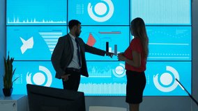 4K Business man & woman in office, looking at video wall with graphs & data Dec 2016-UK