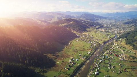 4K Aerial Drone Footage View: Flight over sunny village with houses, forests, fields road and river in sunset soft light. Carpathian Mountains, Ukraine, Europe. Majestic nature landscape. Beauty world