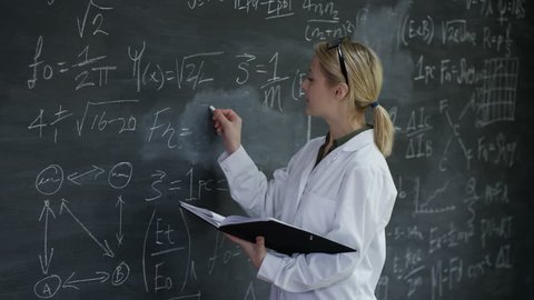 4K Portrait smiling woman in white coat writing math formulas on blackboard Dec 2016-UK – Stockvideo