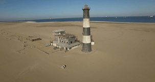 Aerial drone footage of desert sand peninsula, old lighthouse and power station building on ocean seals beach, Walvis Bay lagoon view with sea background and ships at Namibia's Atlantic west coast