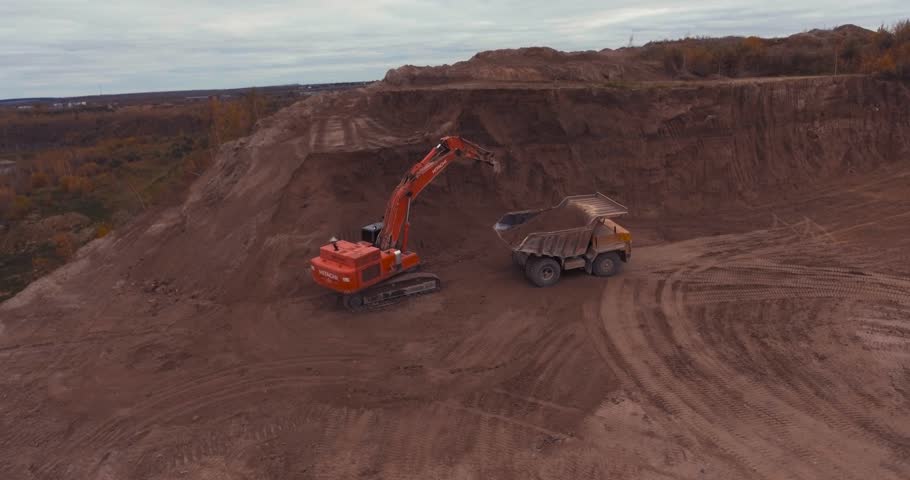 Flight to drone on sand quarry with heavy machinery, the old truck and excavator. loading sand excavating in heavy trucks