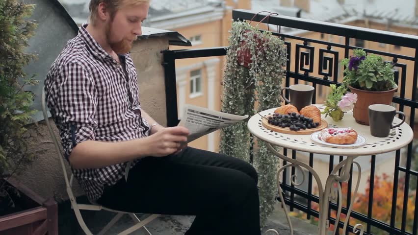 Man With Cup of Coffee Reading a Newspaper on the Balcony Overlooking the City