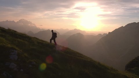 Aerial - Epic shot of a man hiking on the edge of the mountain as a silhouette in beautiful sunset