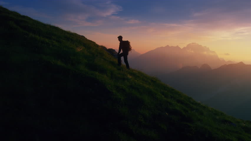Aerial - Epic shot of a man hiking on the edge of the mountain as a silhouette in colorful sunset (edited version) | Shutterstock HD Video #22952899