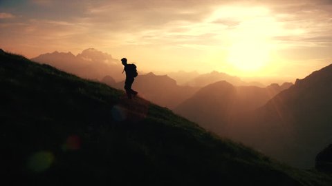 Aerial - Epic shot of a man hiking on the edge of the mountain as a silhouette in beautiful sunset (edited version)