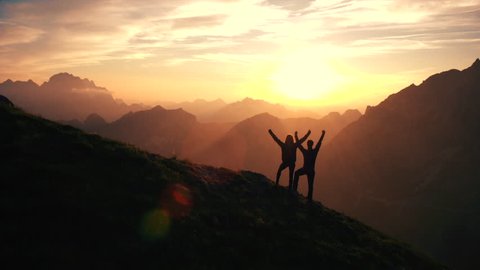 Aerial, edited - Rising above hiking couple celebrating successful climb on the mountain with raising arms at beautiful sunset