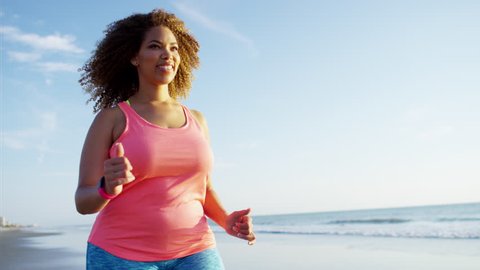 Happy afro hair African American female speed walking along the beach at sunrise for healthcare fitness training RED DRAGON