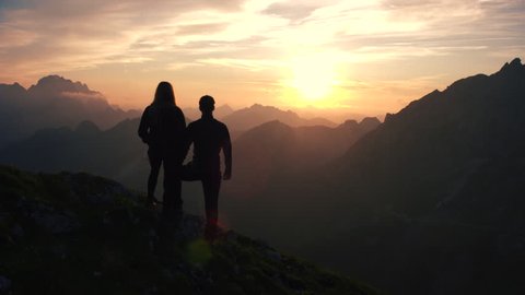 Aerial, edited - Raising above hiking couple watching and admiring beautiful sunset in the mountains