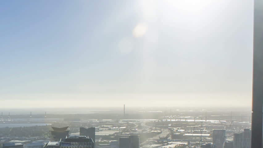 An aerial view of Melbourne cityscape including Yarra River and Victoria Harbour in the distance. Time lapse during sunset with beautiful sun ray bursting through fast moving clouds. Zoom out