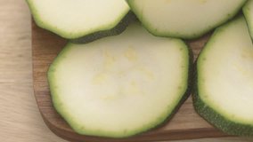 Sliced zucchini on wooden cutting board. Food preparation film clip. Concept of vegetarian cooking.