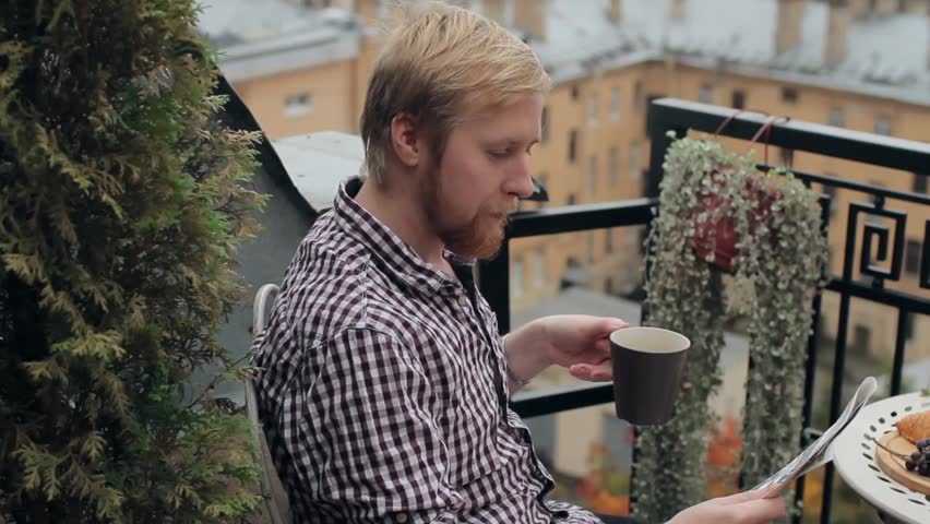 Man With Cup of Coffee Reading a Newspaper on the Balcony Overlooking the City