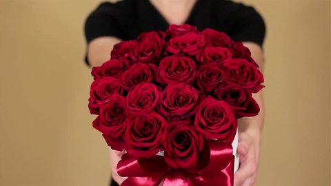 Man in black t shirt holding in hand rich gift bouquet of 21 red roses. Composition of flowers in a white hatbox. Tied with wide red ribbon and bow. In slow motion