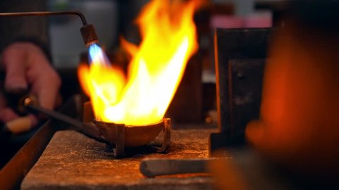 Goldsmith melting gold to liquid state in crucible with gasoline burner