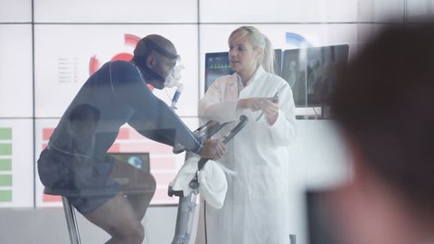 4K Sport scientist in white coat assessing fitness of man on exercise bike Dec 2016-UK