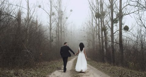 Happy young newlyweds are walking in a forest and they kiss, slow motion. 4k