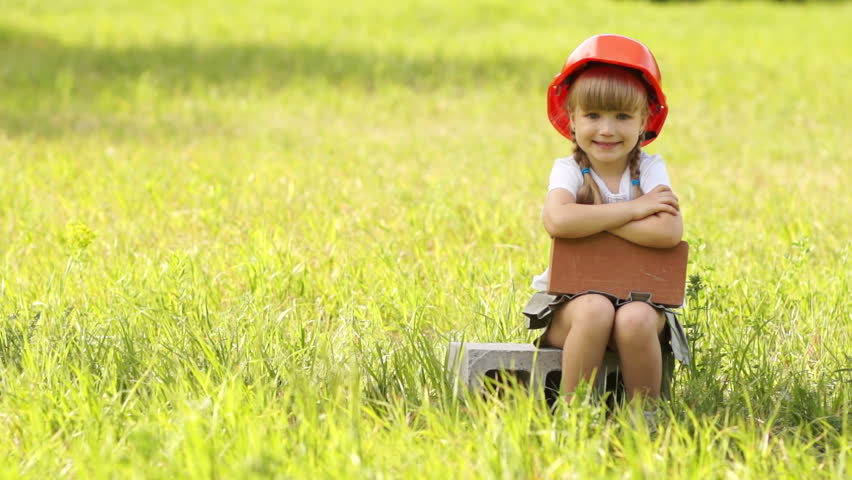 Girl in hard hat sitting on cinder block gives thumbs up