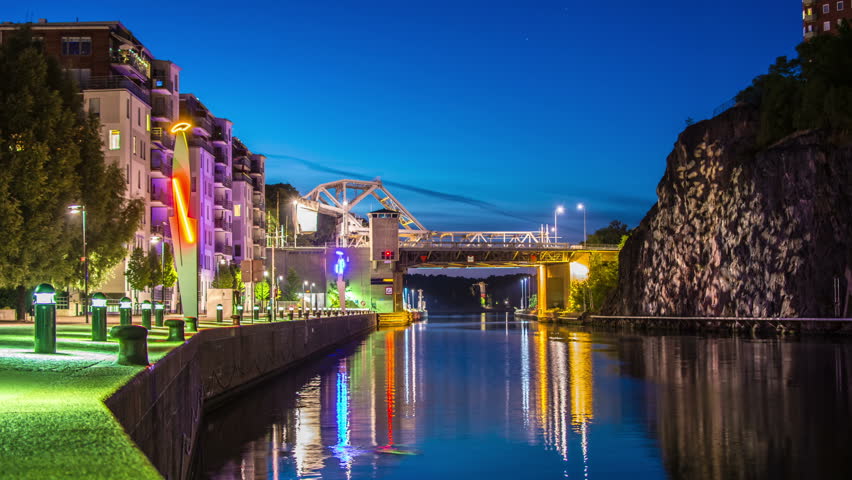 Time Lapse of canal and bridge at night. Traffic passing by over bridge and boat passing in canal, apartment buildings