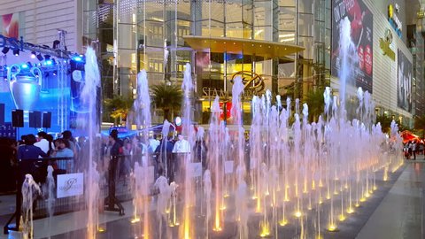 BANGKOK, THAILAND - 3 MAR 2016: amazing cascade fountain illuminated by colorful lights, people walking down city street and shopping mall Siam Paragon on background. Side view. Camera stays still.