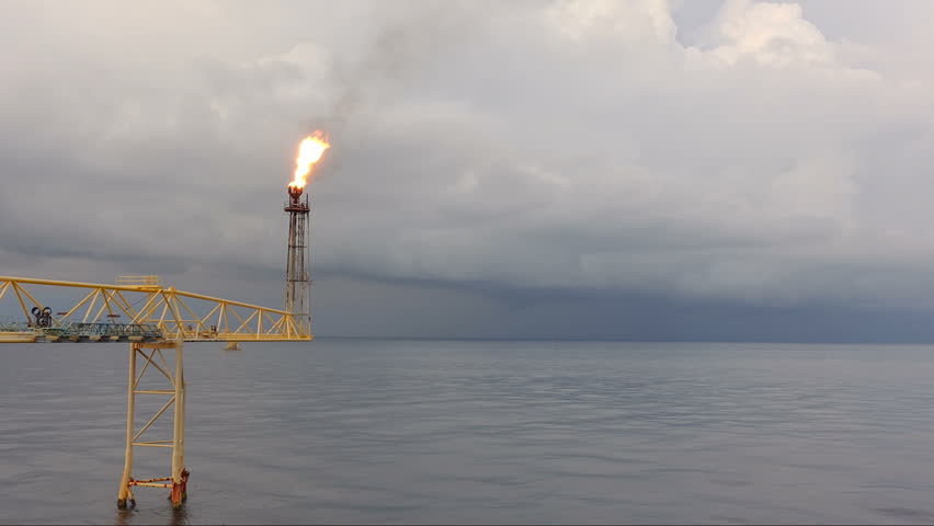 Timelapse  footage of oil and gas platform with flare burning with dark clouds of storm in zoom out view 