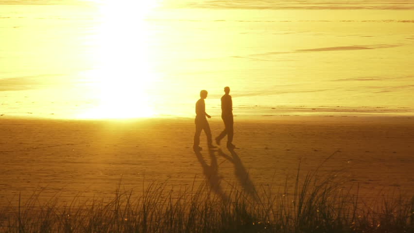 Two people walking during sunset at beach, dissolve into the sunlight reflection