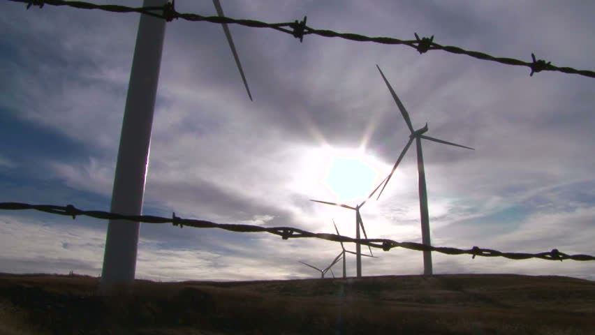 Wind turbines sit still on calm and sunny day in Washington with barbed wire in