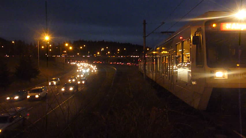 Rush hour traffic at night with metro train traveling on rail stop and go.
