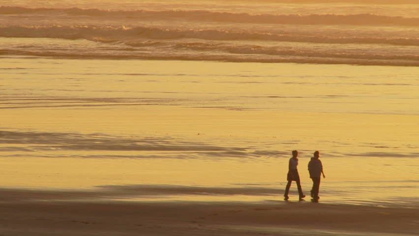 Pacific Ocean sunset during beautiful sunset with two people walking sandy