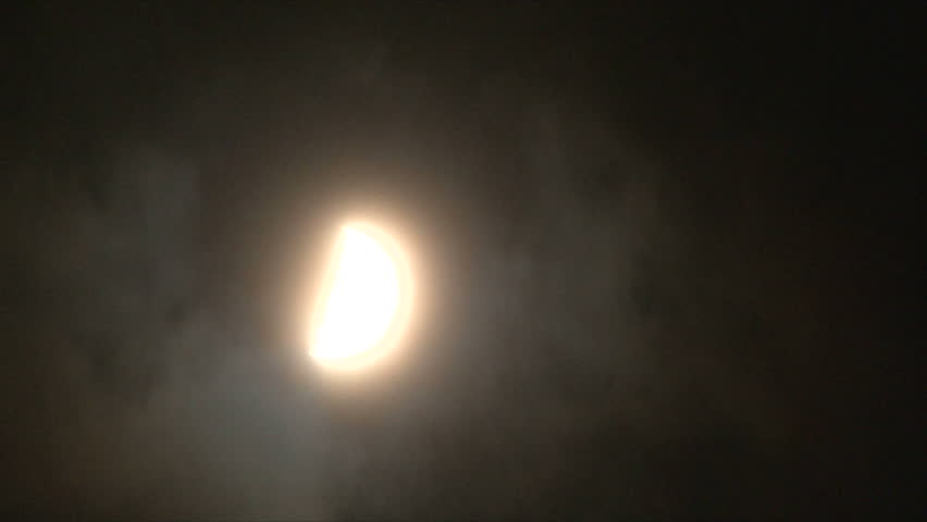 Glowing half moon at night disappears in night clouds.