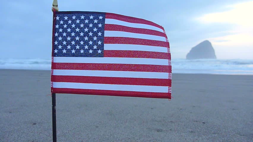 United States of America flag waving on the sands of the Pacific Ocean.