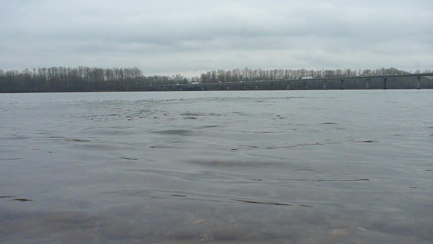 Nature scenic with long bridge with traffic over river and rocks being skipped.