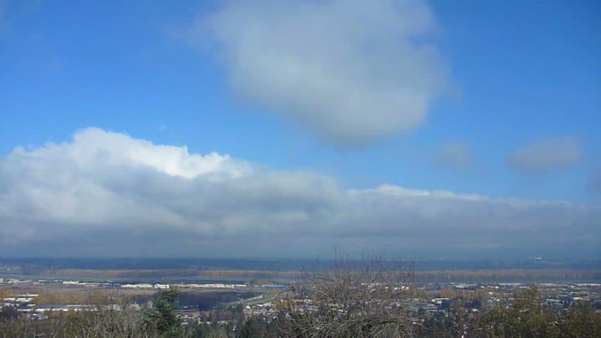Clouds move over urban sprawl in Portland, Oregon on blue sky day time lapse.
