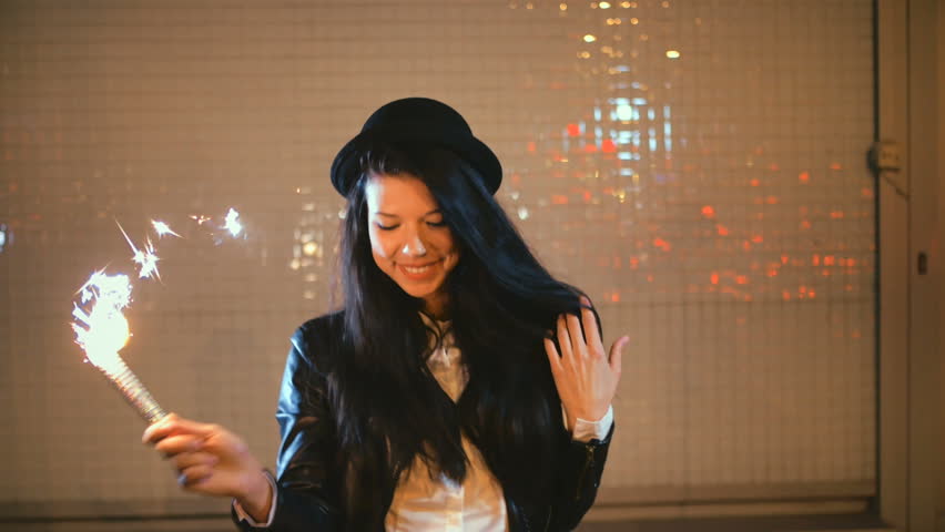 Cheerful womn dancing in night city with bengal fire sparkler in her hands toned shot